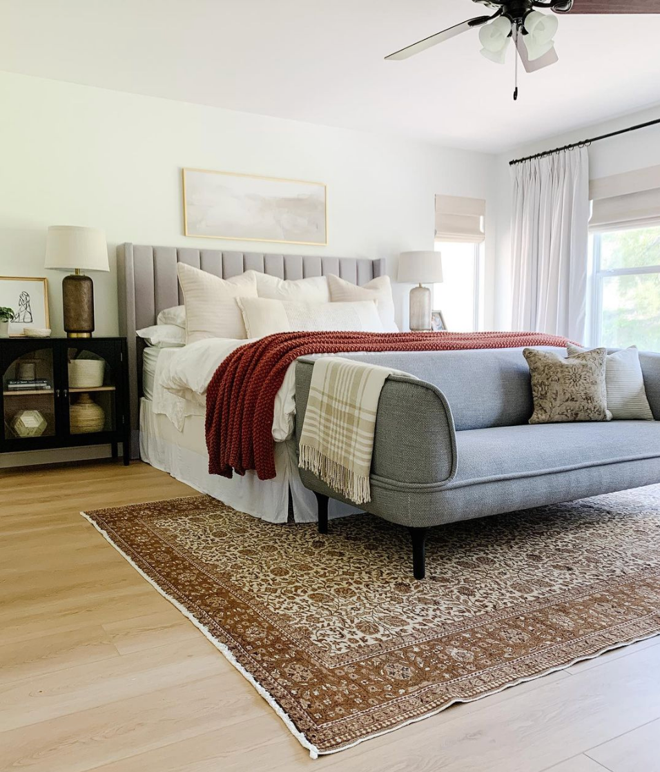 A bright bedroom with a gray sofa at the foot of the bed and Blue Heaven on the far wall