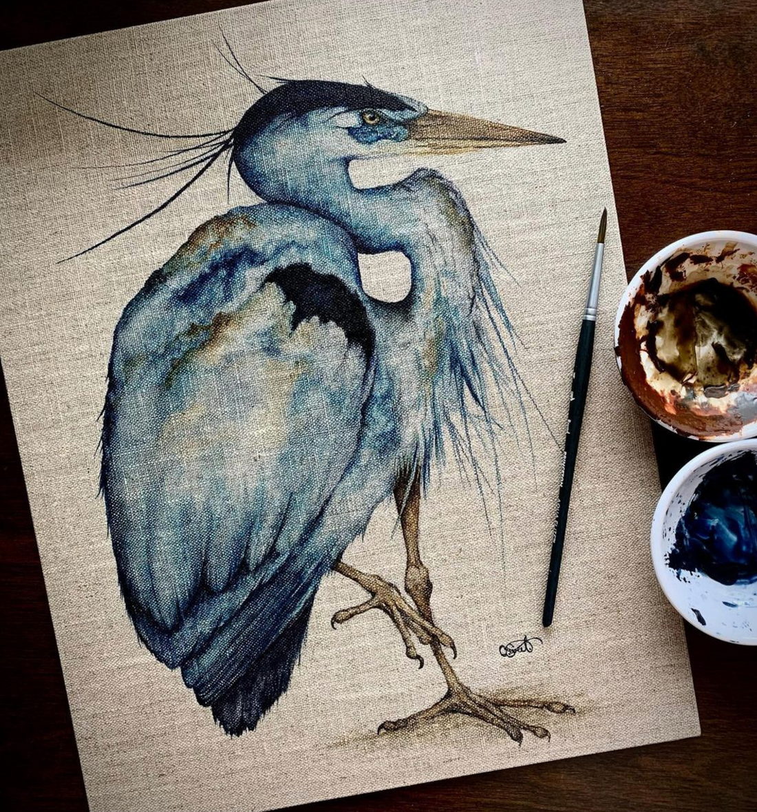 A great blue heron watercolor on linen, with brush and paint cups beside it